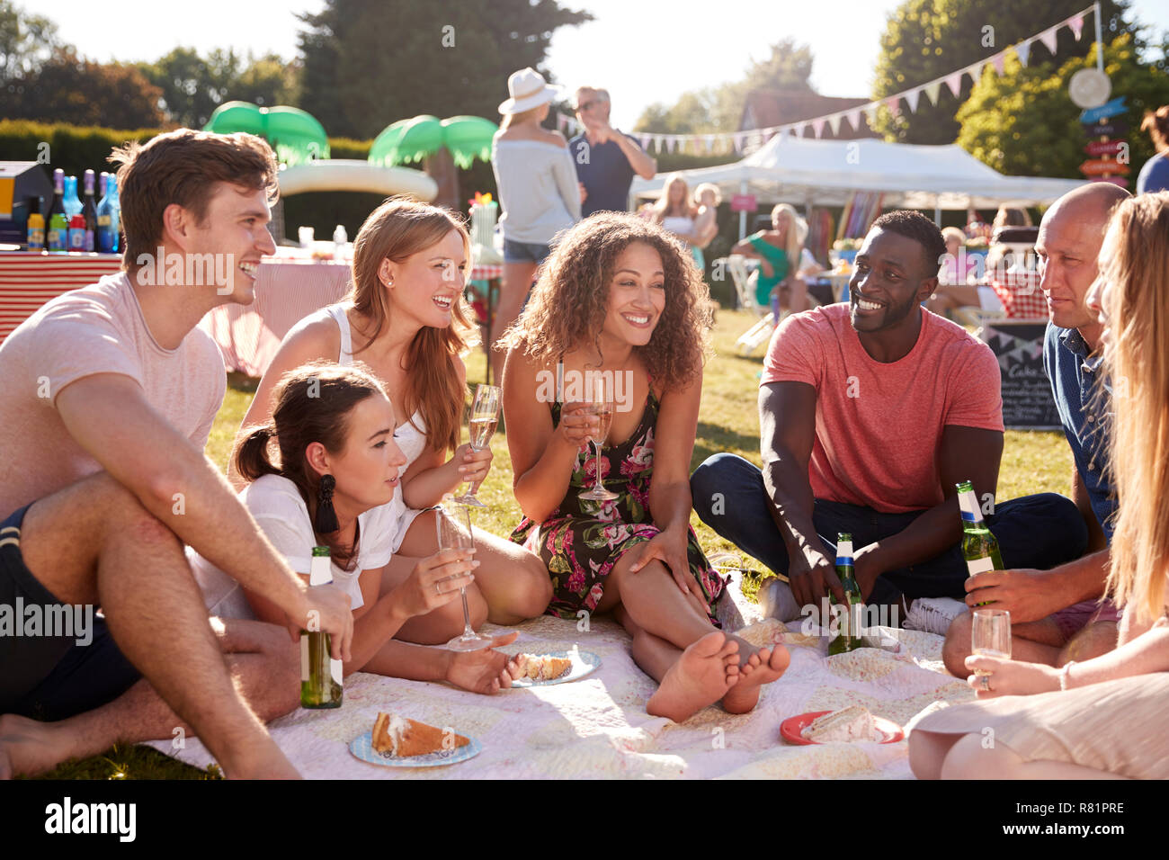 Gruppe von Freunden sitzen auf Teppich bei Sommer Garten Fete mit Getränken Stockfoto