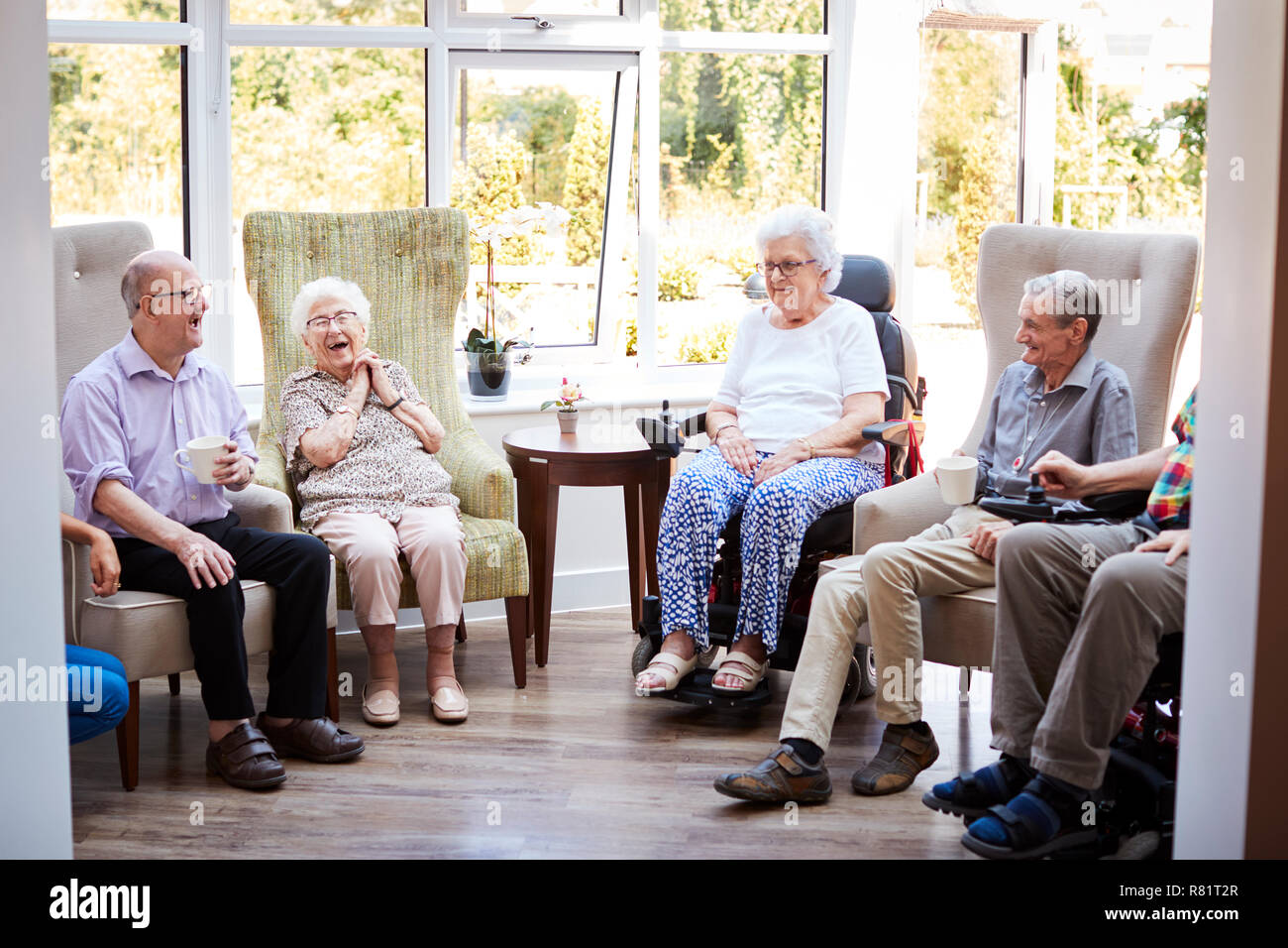 Männliche und weibliche Bewohner Sitzen in Stühlen und Gespräch in der Lounge des Seniorenheims Stockfoto