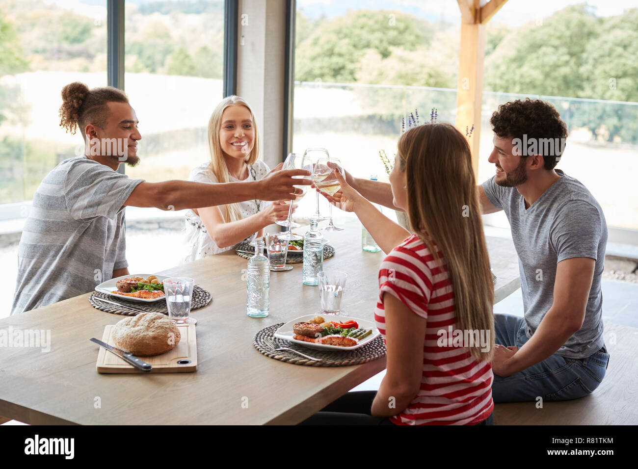 Vier junge erwachsene Freunde feiern bei einem Abendessen ihre Weingläser anheben, in der Nähe Stockfoto