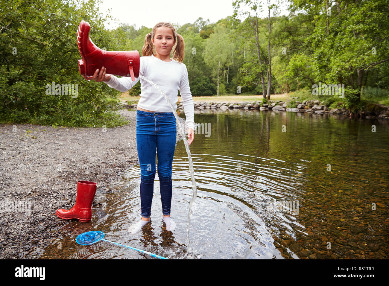 Junges Mädchen stehen in einem Fluss Socken tragen gießt Wasser aus ihrem roten Wellington boot Stockfoto