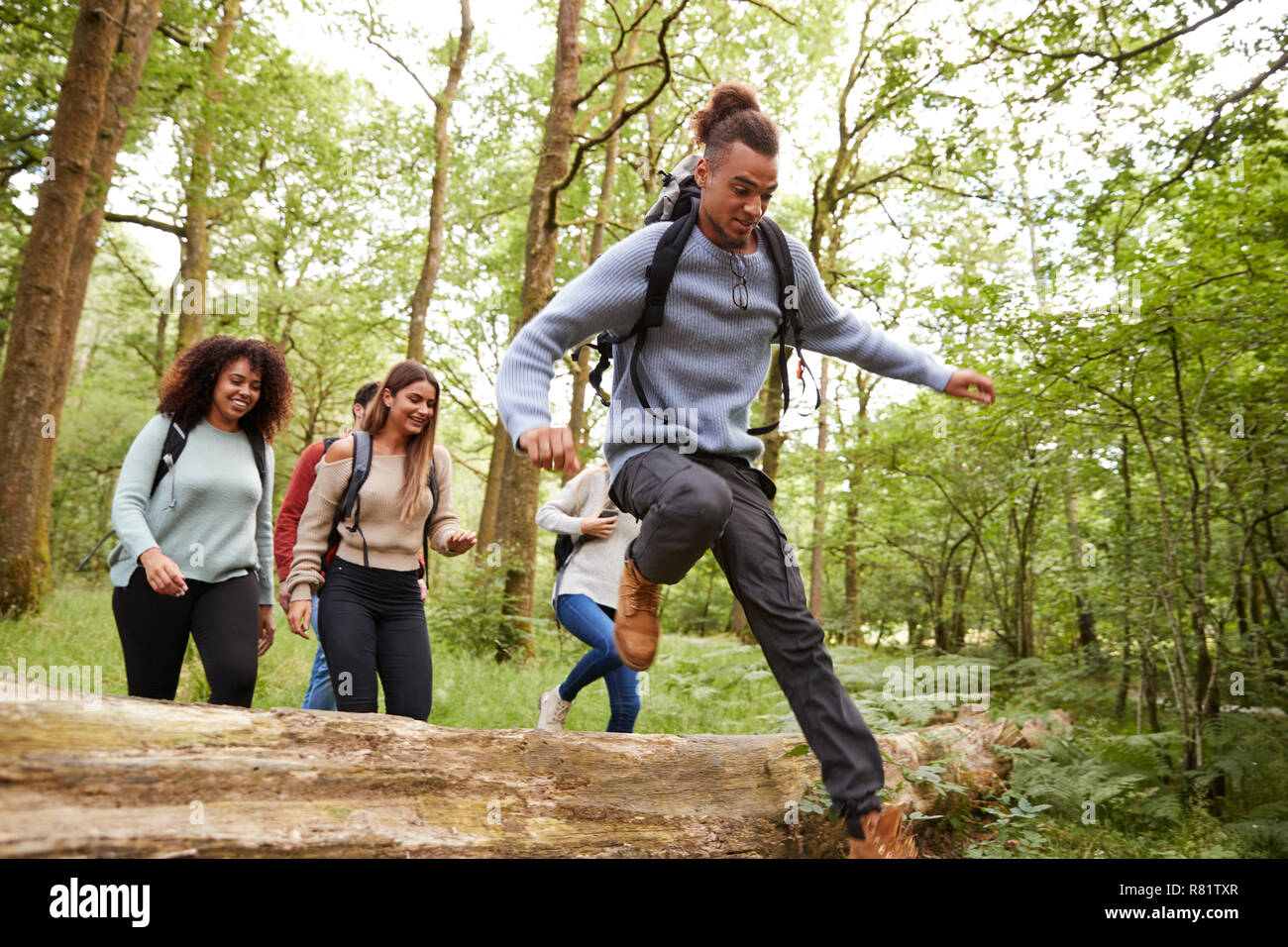 Multi-ethnische Gruppe von fünf jungen Erwachsenen Freunde läuft in einem Wald und springen über umgefallene Baum während einer Wanderung Stockfoto