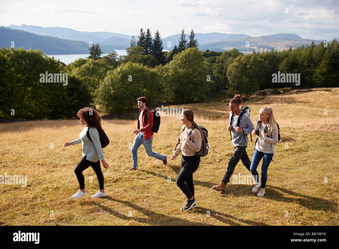 Eine Gruppe von fünf jungen Erwachsenen Freunde Lächeln beim Gehen auf eine ländliche weg während einer Bergwanderung, Seitenansicht Stockfoto