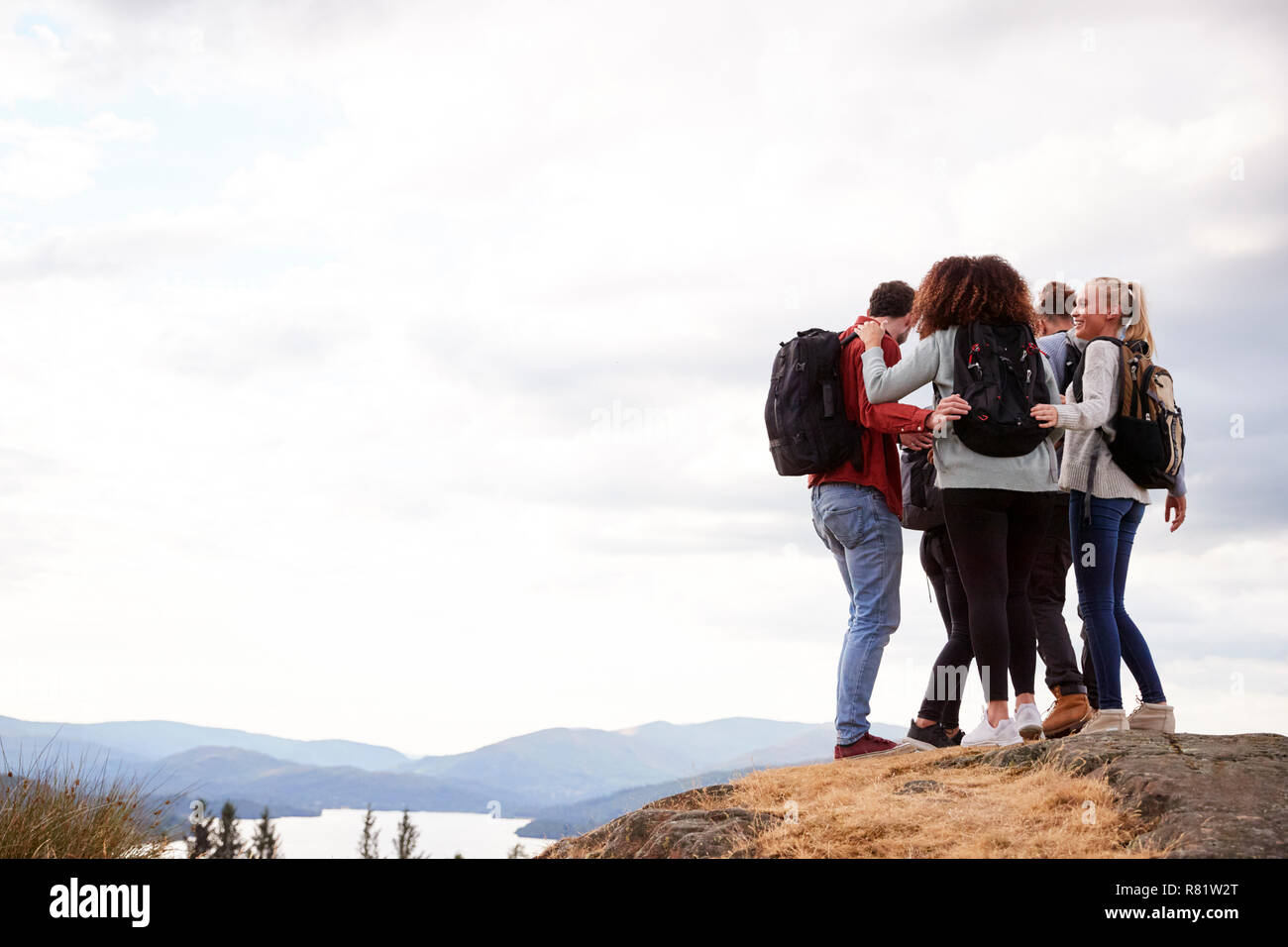Eine Gruppe von fünf gemischten Rennen junge erwachsene Freunde umarmen nach Ankunft auf dem Gipfel während der Wanderung, in der Nähe Stockfoto