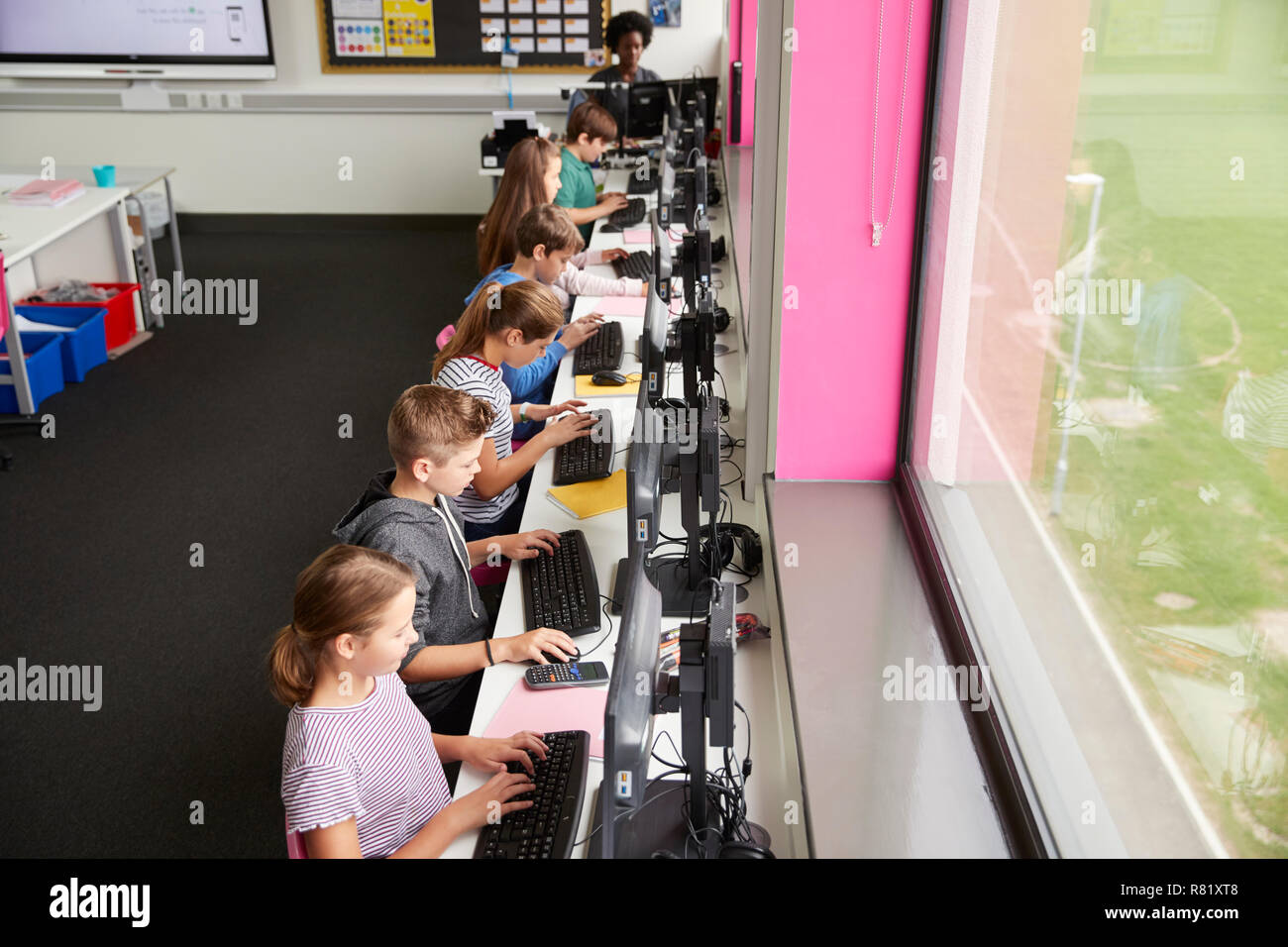 Linie der High School Kursteilnehmer an Bildschirmen in Computer Klasse mit Lehrerin im Hintergrund Schuß von hohen Winkel Arbeiten Stockfoto