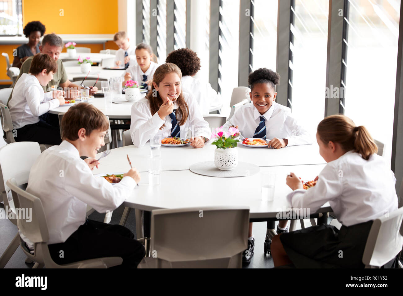 Gruppe von Schülerinnen und Schüler tragen Uniform Sitzen um den Tisch und Essen Mittagessen in der Cafeteria Stockfoto