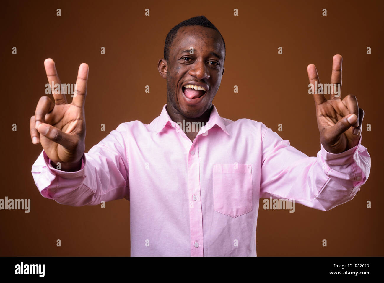 Porträt der jungen afrikanischen Geschäftsmann Making Peace Zeichen gegen braunen Hintergrund Stockfoto
