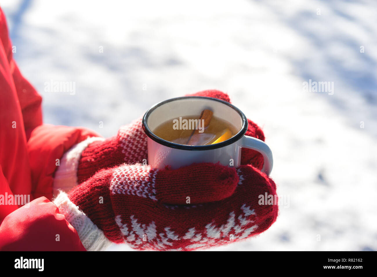 Hände auf Gestrickte Handschuhe Holding dampfende Tasse heißen Tee auf Verschneiten Wintermorgen im Freien. Frau hält Gemütliche festliche rot Tasse mit einem warmen Getränk am Weihnachtsmorgen Stockfoto