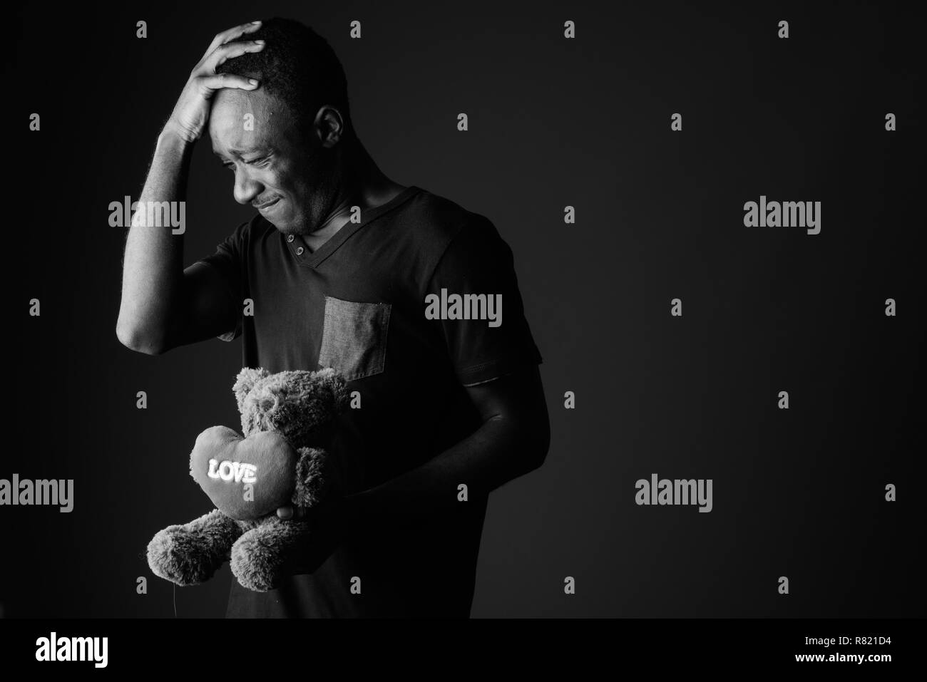 Traurige junge afrikanische Mann mit Teddybär und der Liebe Zeichen Text in Kopfschmerzen Stockfoto