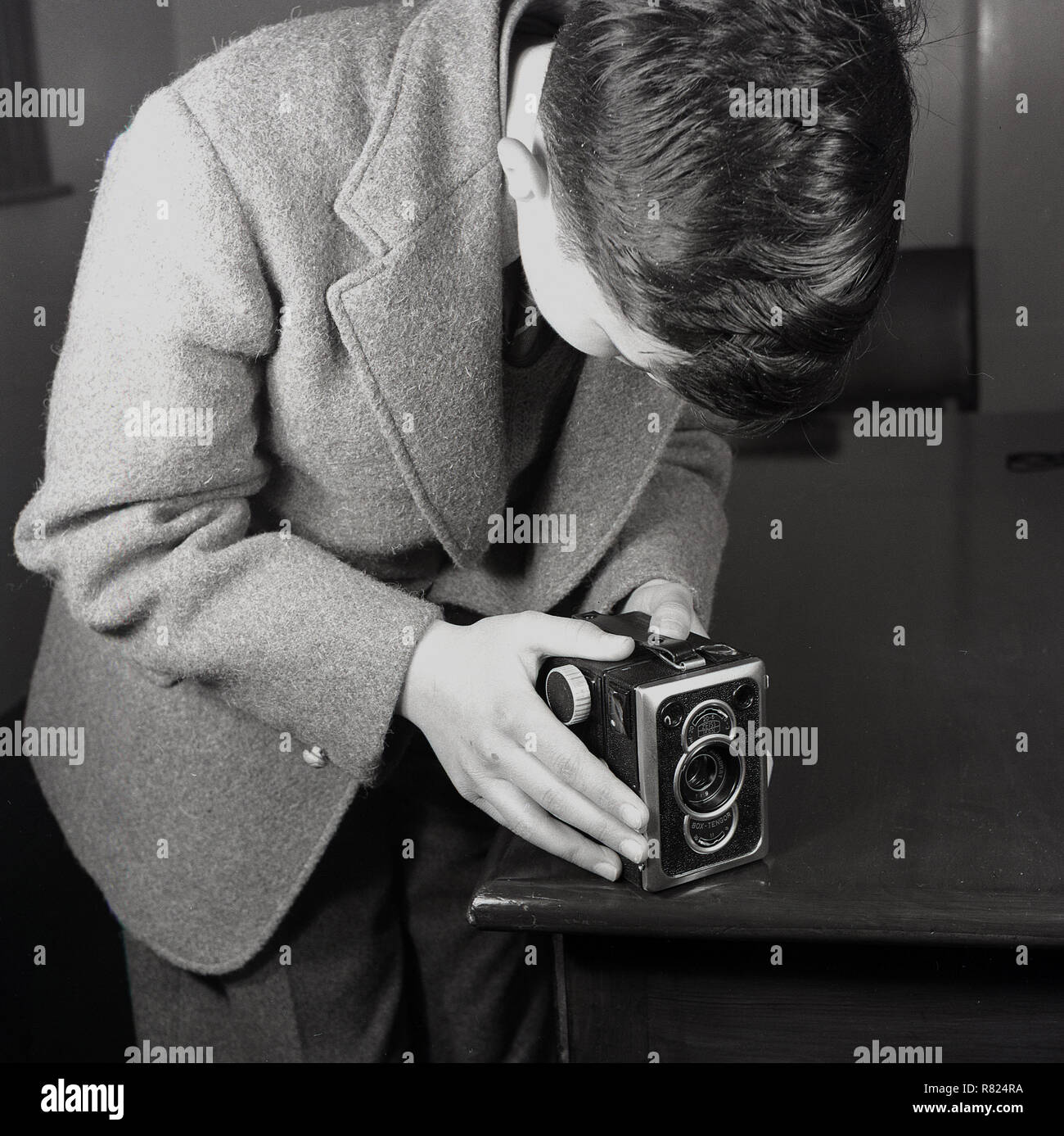 1950, historische Fotografie.. ein schuljunge trägt eine Wolljacke mit der Ecke eines hölzernen Tisch als Unterstützung für seine box Tengor Mittelformat film Kamera von Zeiss Ikon in den frühen 50er Jahren gemacht, der Typ 56/2 war ein gut gebauter und relativ fortgeschrittenen, Kamera, als "König der "Kameras". Stockfoto