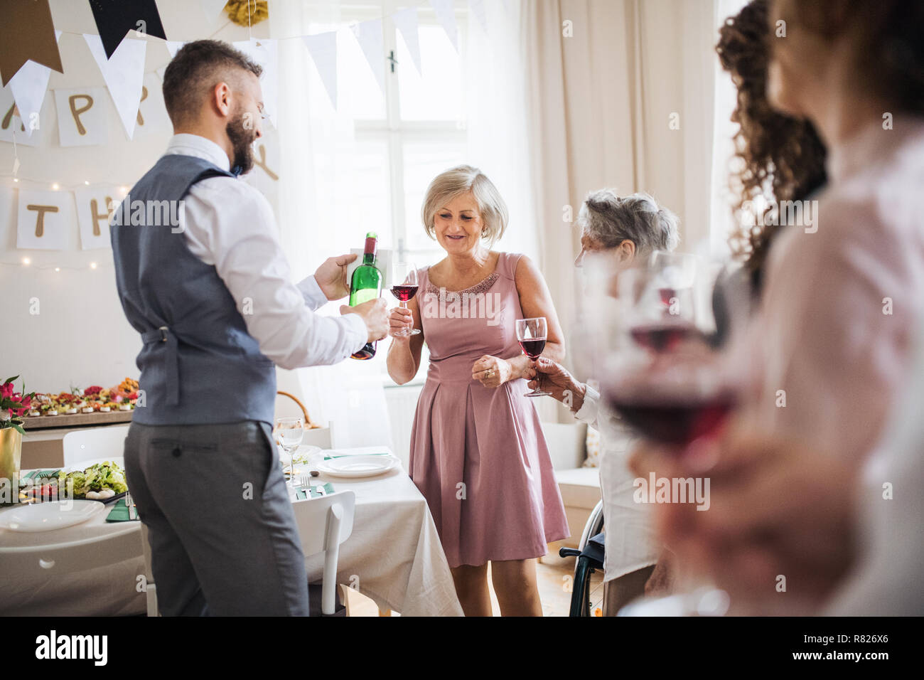 Ein Mann gießen Gäste Wein an einem indoor Geburtstagsfeier in der Familie. Stockfoto