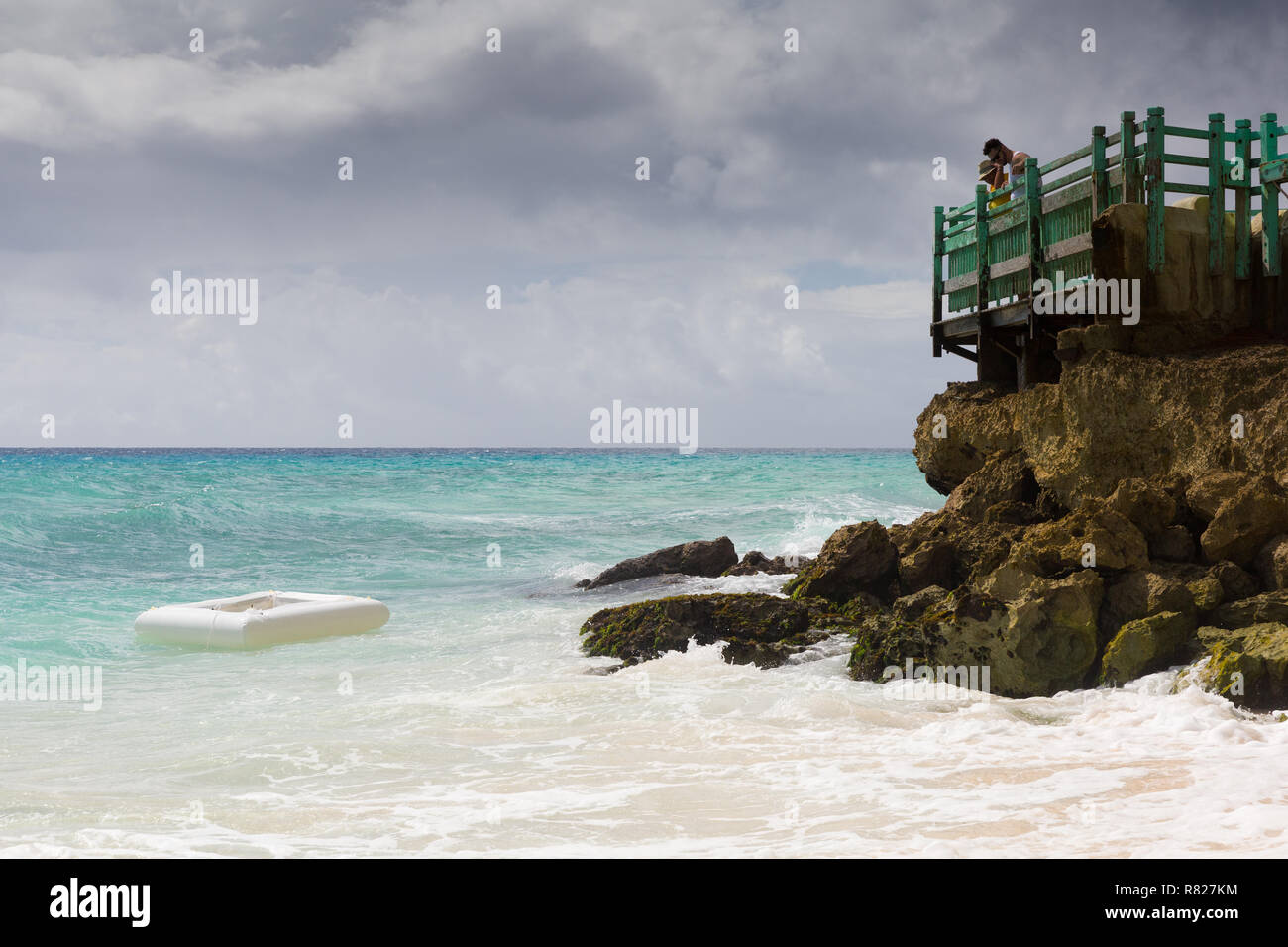Eine weggeworfene Kunststoff Rettungsinsel wäscht bis auf den Felsen auf der karibischen Insel Barbados während Urlauber bei einem Resort Hotel Blick auf. Stockfoto