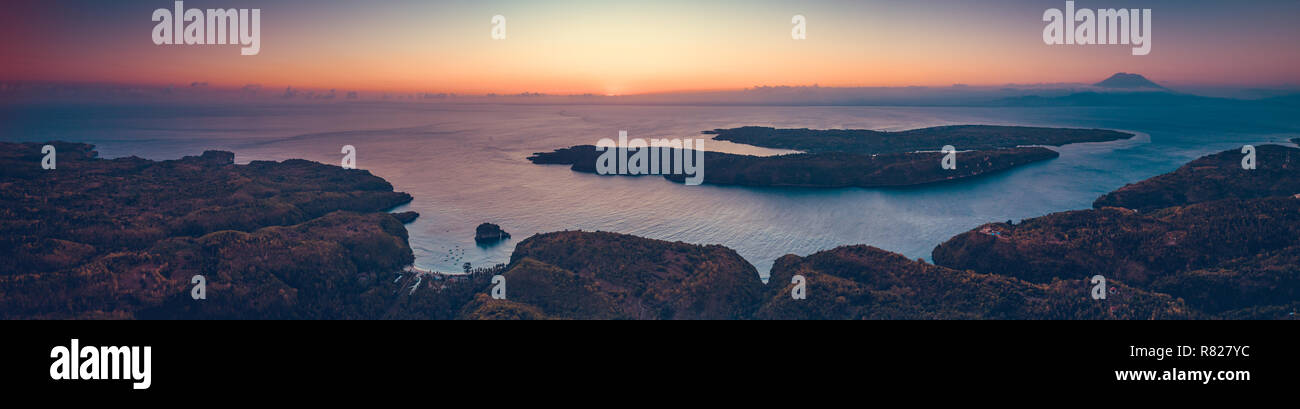 Sonnenuntergang panoramischen Überblick über Indonesien Küste und das Meer. Antenne drone Schuß des Asiatischen wilde Natur. Atemberaubende Landschaft. Sonnenuntergang über der Indonesischen land und ruhigen Meer. Leuchtend bunte Himmel. Stockfoto