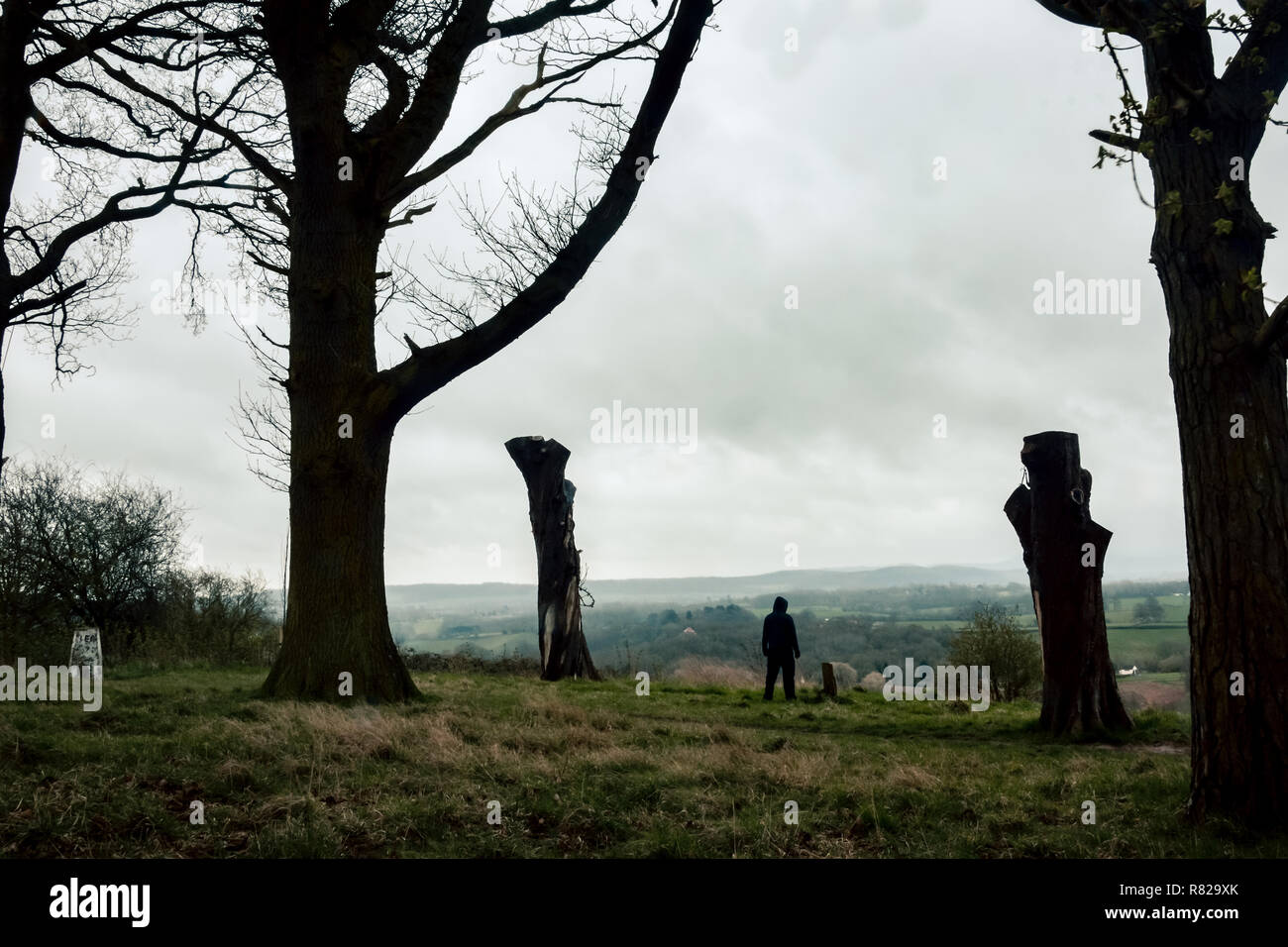 Ein einsamer Moody hooded Abbildung steht auf einem Hügel, mit Blick auf die englische Landschaft im Winter. Stockfoto