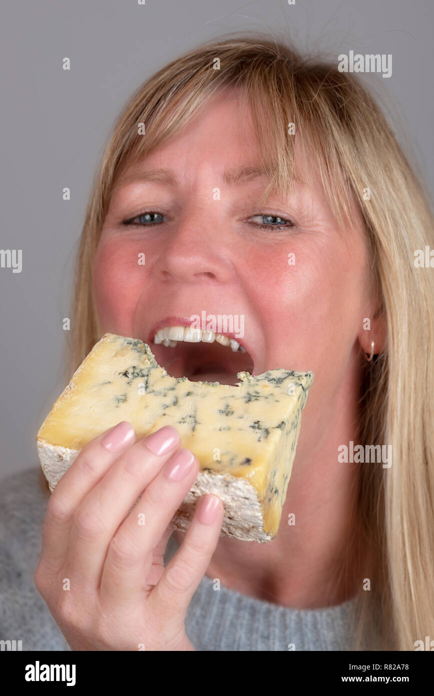 Blonde Frau essen und genießen Sie ein Keil der blauen Käse Stockfoto