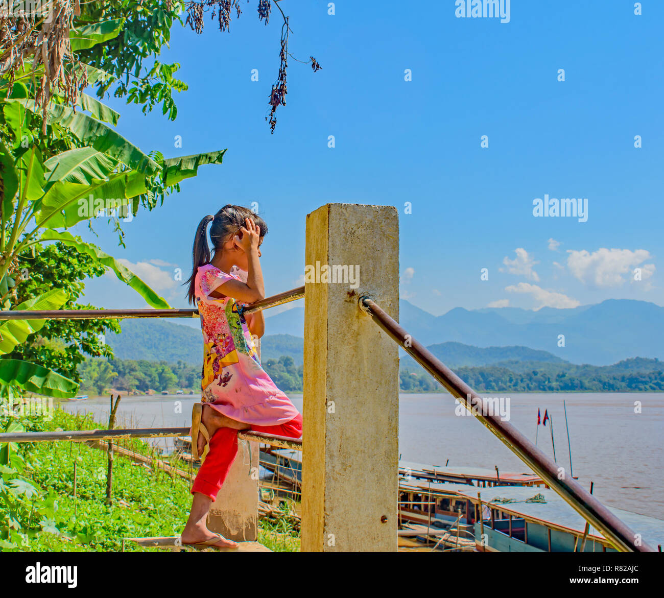 Ein kleines Mädchen lehnte sich auf dem Geländer durch ein Dorf am Mekong River sieht und denkt, 'Eines Tages mein Schiff wird kommen' Stockfoto