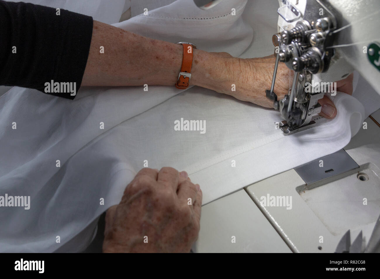 Eine Nahaufnahme Vorderansicht eines Damenhände Aussaat weiß Leinen Stoff auf eine industrielle Maschine Stockfoto