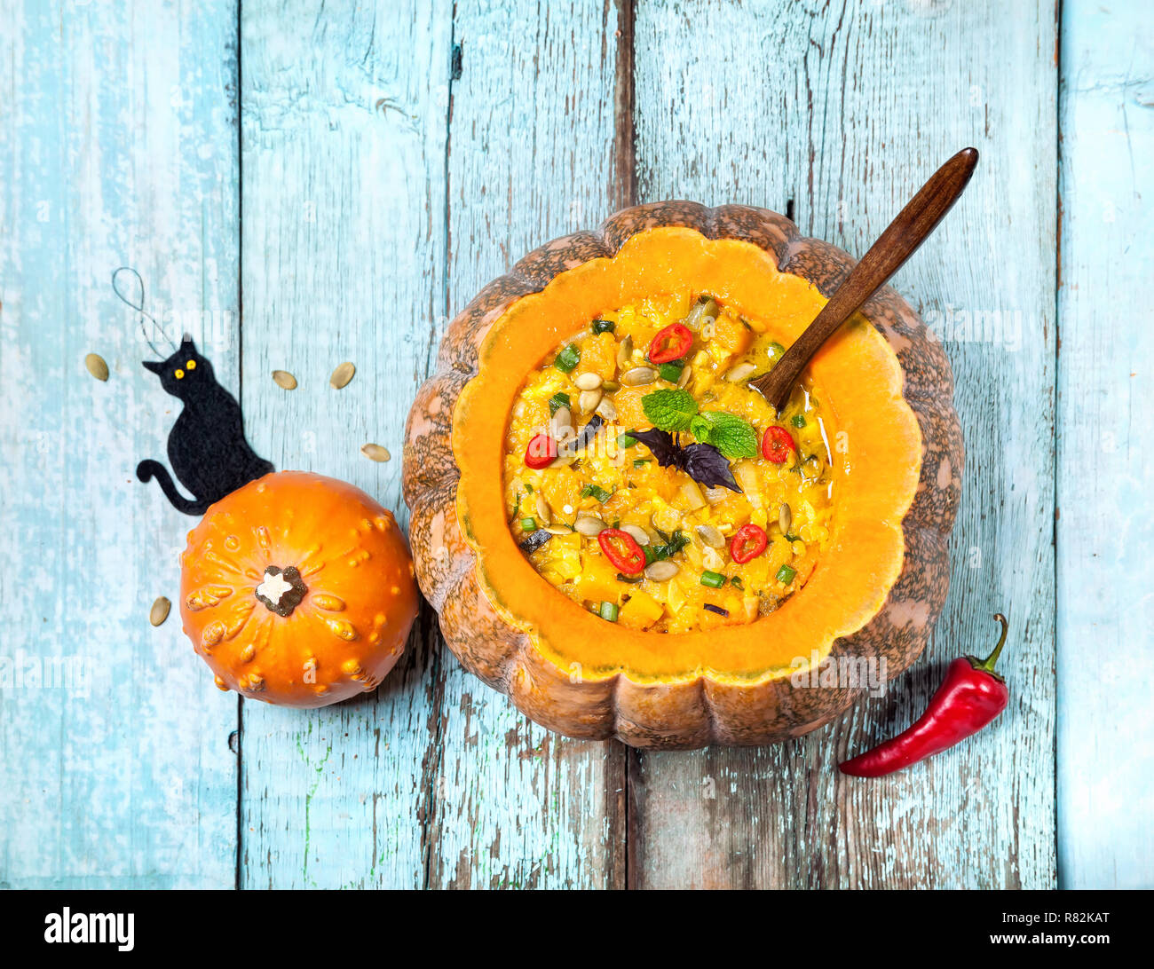 Suppe mit Linsen in den geschnitzten Kürbis und schwarze Katze spielzeug auf dem blauen Hintergrund Holz an Halloween Party Stockfoto