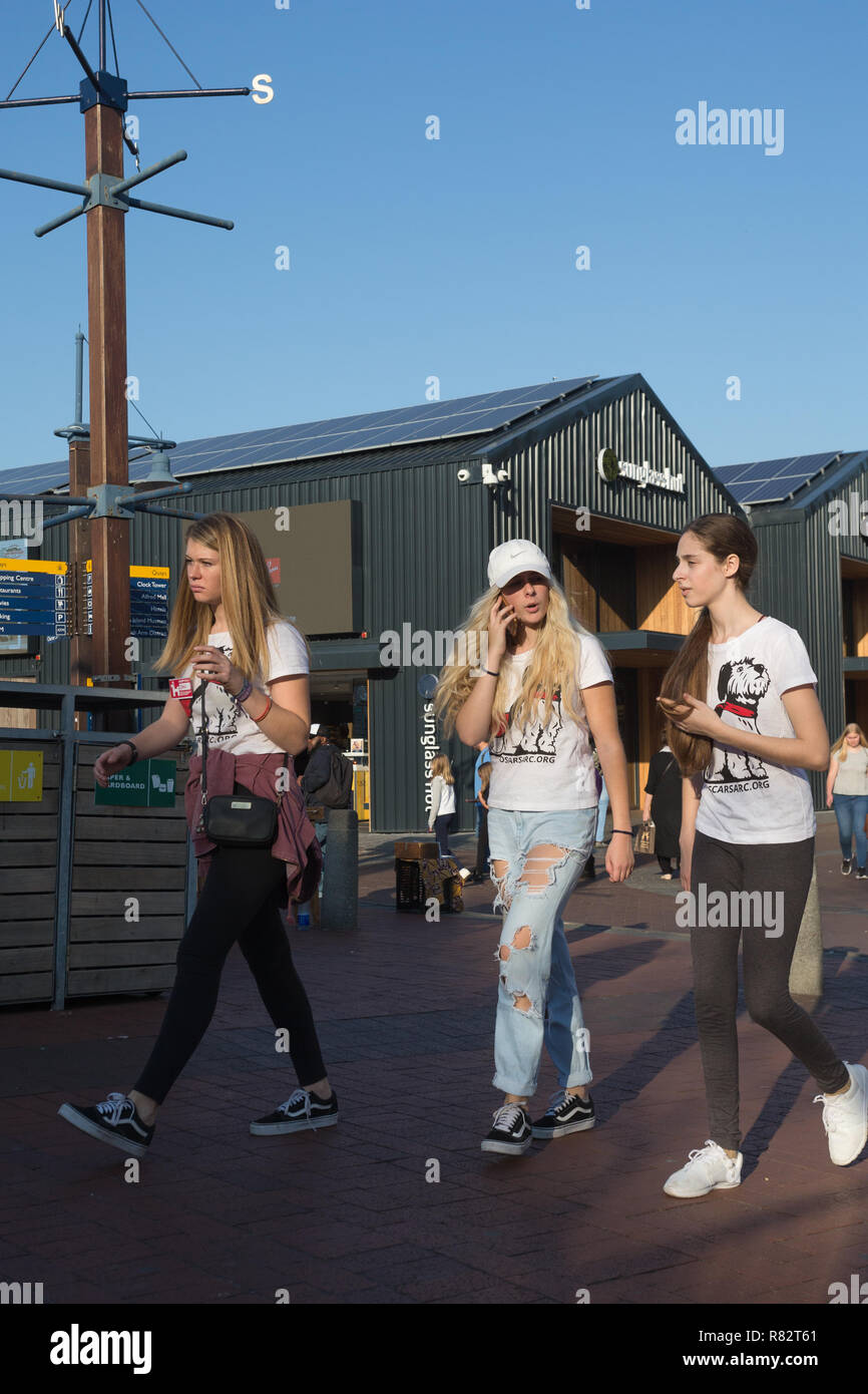 Junge Mädchen oder Teenager, zusammen gehen, während ein Gespräch über Ihr Mobiltelefon ist, stilvolle Street Fashion bei V&A Waterfront in Kapstadt Stockfoto