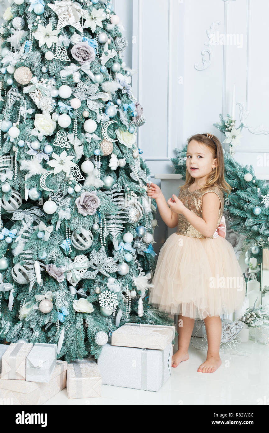 Kleines Mädchen in einem schönen Kleid steht in der Nähe ein Weihnachtsbaum. Sie ist überrascht. Stockfoto