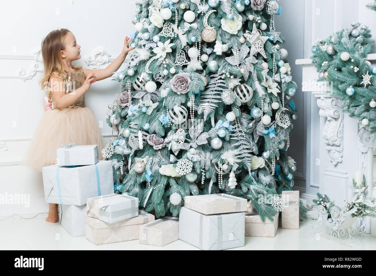 Kleines Mädchen in einem schönen Kleid hängt, Dekorationen auf den Weihnachtsbaum. Stockfoto