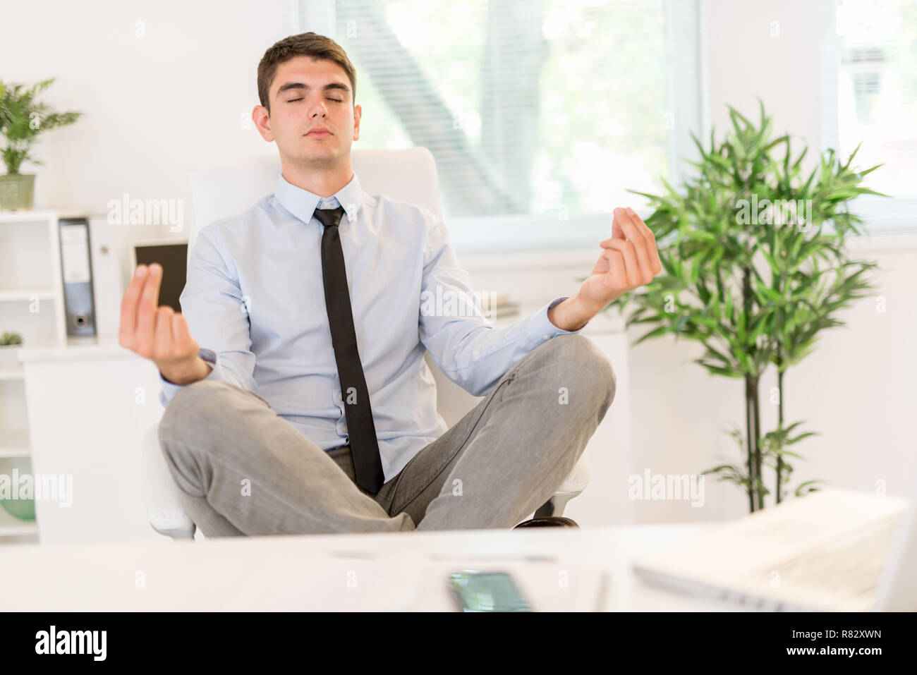 Junge Unternehmer Üben Yoga im Büro. Er sitzt auf Lotus in einem Stuhl vor ihrem Schreibtisch darstellen. Stockfoto