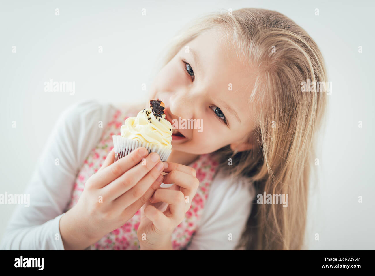 Schöne glückliche kleine Mädchen beißen Geburtstagskuchen. Mit Blick auf die Kamera. Stockfoto