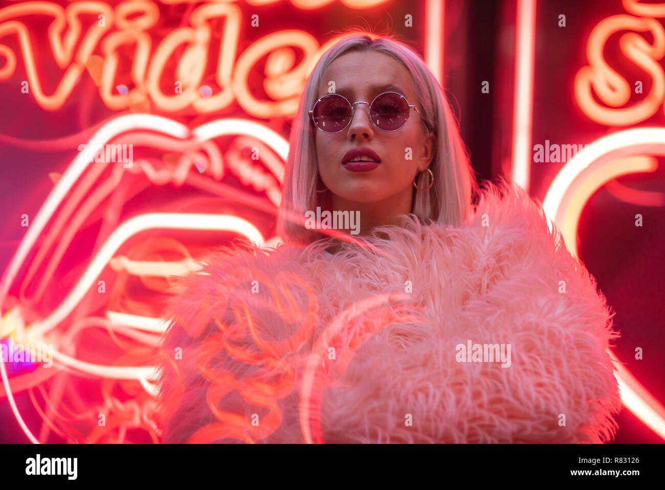 Filmisches Porträt der blonde Mädchen mit pelzigen rosa Mantel auf Leuchtreklame bei Nacht Stockfoto