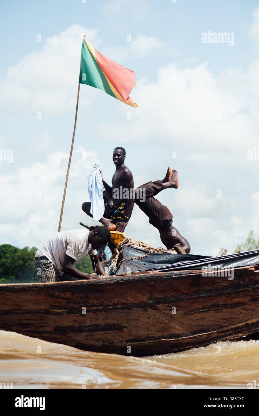 Mali, Afrika. Schwarze junge Männer angeln glücklich auf dem Holz Händler Boote auf dem schmutzigen Fluss Niger. Mali Flagge auf dem Boot Stockfoto