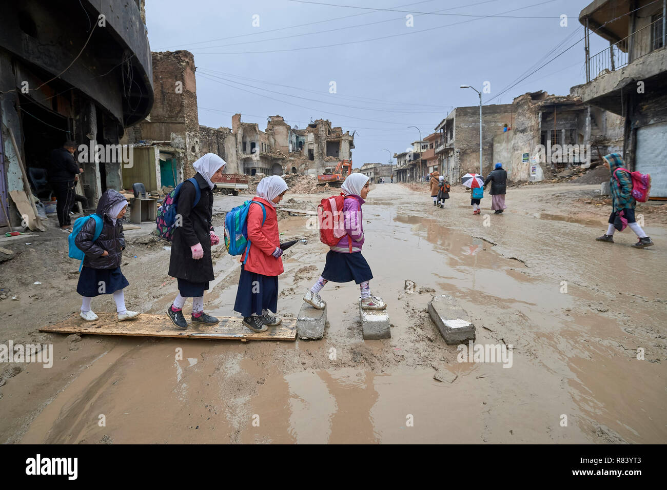 Mädchen Navigieren in einer schlammigen Straße, als Sie zu Fuß inmitten der Trümmer der Alten Stadt Mosul, Irak, die in den Krieg gegen ISIS verwüstet wurde, in die Schule zu gehen. Stockfoto