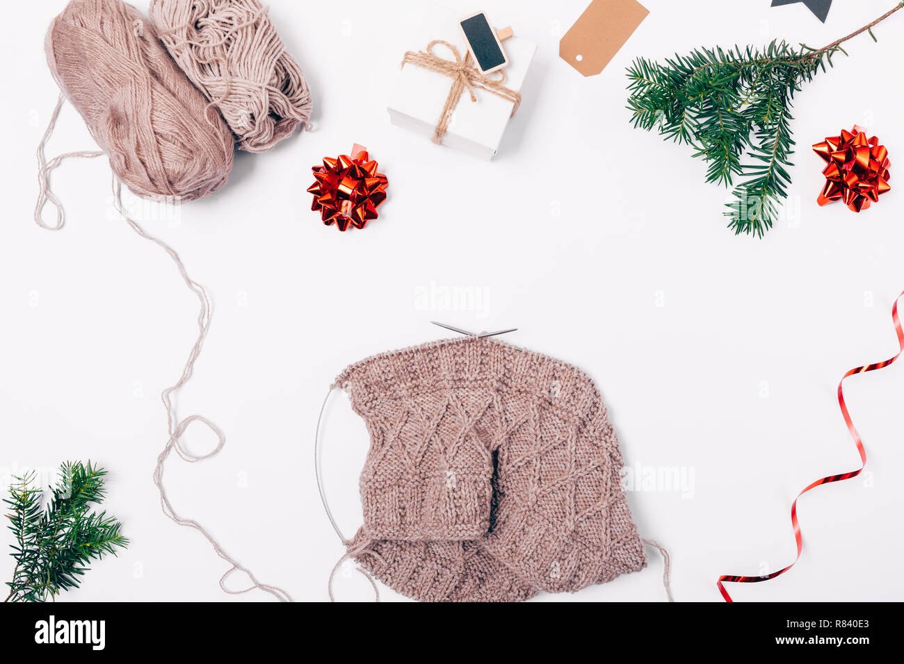 Flach Zusammensetzung handgefertigte gewirkten Tuch aus natürlichen Wolle neben Geschenkbox, Weihnachten rote Ornamente und tanne Zweig, Ansicht von oben auf weißer Tisch. Stockfoto