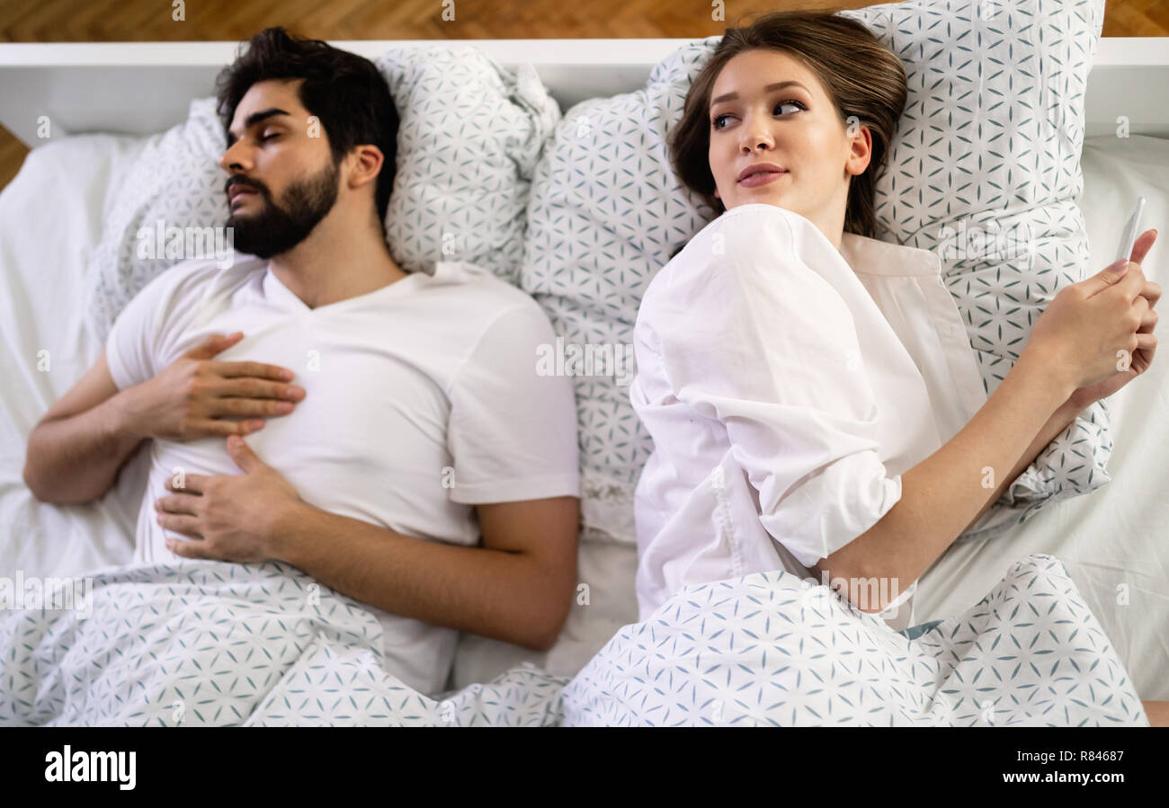 Frau ihre mobile während ihr Mann schlafend auf dem Bett im Schlafzimmer Stockfoto