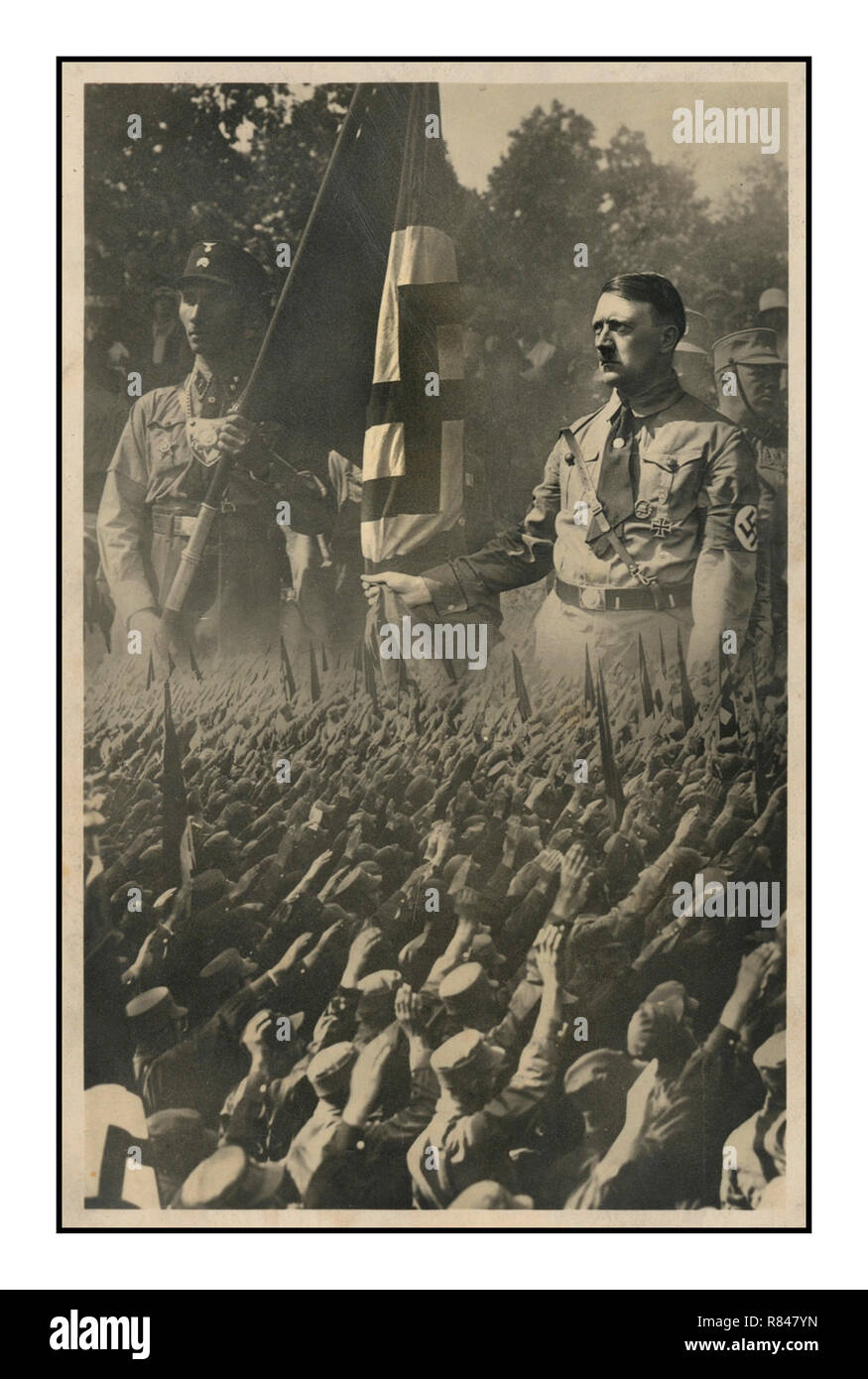 Jahrgang 1930 Die NS-Propaganda Postkarte zeigt eine Masse der ehrenkompanie Deutschen auf ein vergrößertes Bild von Adolf Hitler mit einem Mitglied der SA (Storm Trooper) Wer hält eine Hakenkreuzfahne überlagert. München, Deutschland, c 1933 von Hoffmann, Hitlers persönlicher Fotograf... SA, Abkürzung für Sturmabteilung (Deutsch: "Assault Division"), beinamen Sturmtruppen oder Braunhemden, Deutsche Sturmtruppen oder Braunhemden, in der deutschen nationalsozialistischen Partei, einer paramilitärischen Organisation, deren Methoden der gewaltsamen Einschüchterungen eine Schlüsselrolle in Adolf Hitlers Aufstieg zur Macht gespielt. Stockfoto Jahrgang 1930 Die NS-Propaganda Postkarte zeigt eine Masse der ehrenkompanie Deutschen auf ein vergrößertes Bild von Adolf Hitler mit einem Mitglied der SA (Storm Trooper) Wer hält eine Hakenkreuzfahne überlagert. München, Deutschland, c 1933 von Hoffmann, Hitlers persönlicher Fotograf... SA, Abkürzung für Sturmabteilung (Deutsch: "Assault Division"), beinamen Sturmtruppen oder Braunhemden, Deutsche Sturmtruppen oder Braunhemden, in der deutschen nationalsozialistischen Partei, einer paramilitärischen Organisation, deren Methoden der gewaltsamen Einschüchterungen eine Schlüsselrolle in Adolf Hitlers Aufstieg zur Macht gespielt. Stockfoto