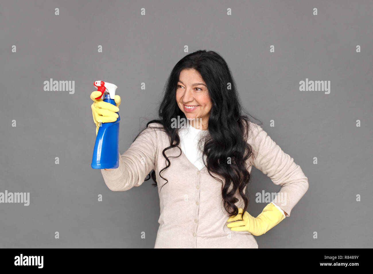 Freestyle. Reife lady in Gummihandschuhe isoliert auf grau Spritzen lächelt Fröhlich stehend Stockfoto