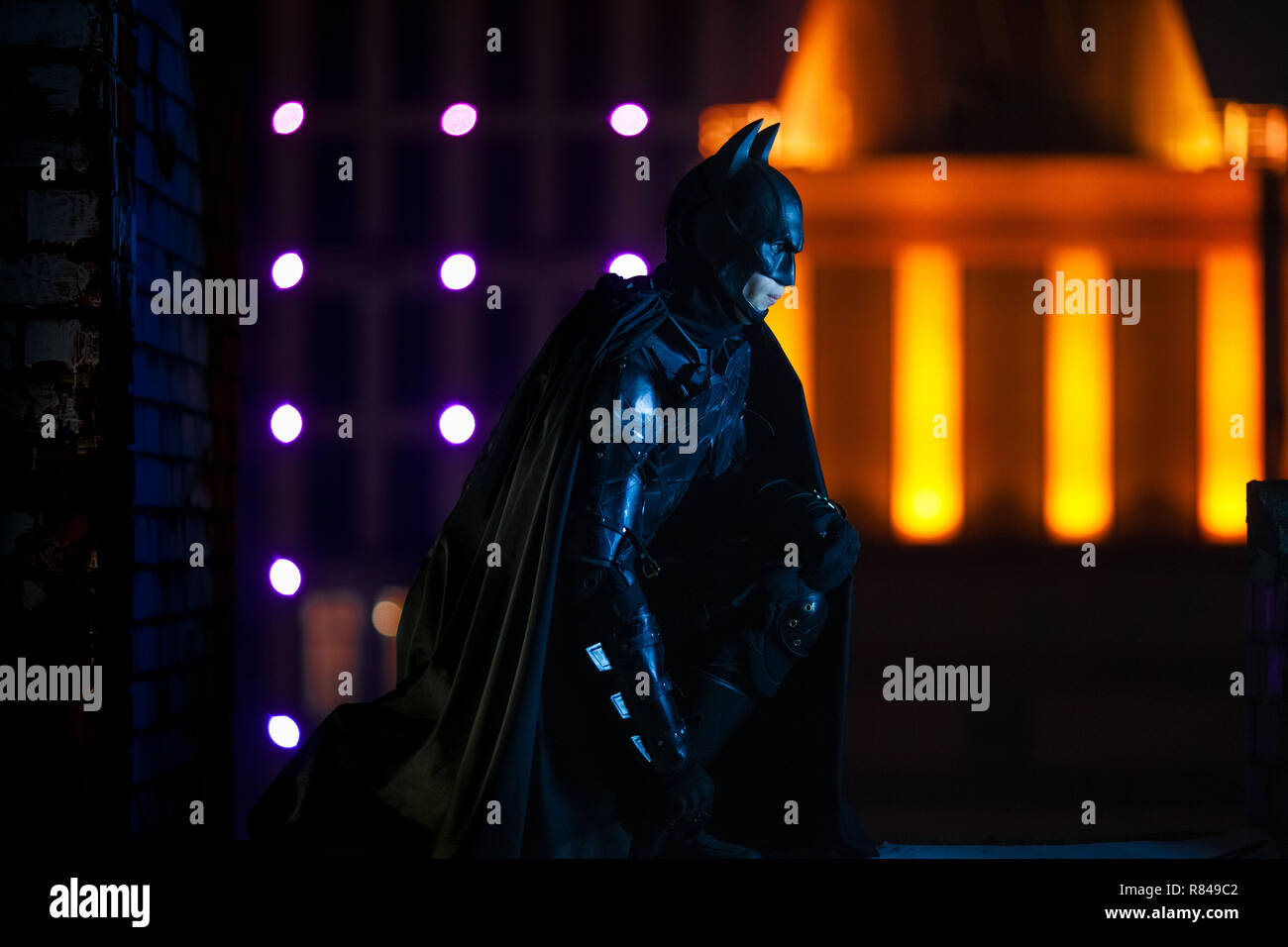 Ein Mann in der Maske, Helm, Rüstung und schwarzen Umhang gekleidet sitzt vor dem Hintergrund der Nacht die Lichter der Stadt und die Gebäude. Cosplay. Stockfoto