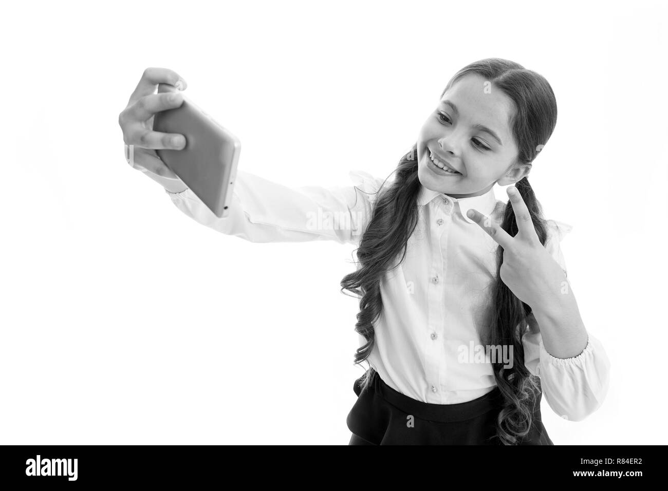 Junge vlogger Stream online. Kind Schuluniform smart Kid glückliches Gesicht. Mädchen niedliche langes lockiges Haar hält Smartphone unter selfie weißen Hintergrund. Kind Mädchen Schule einheitliche Kleidung hält Smartphone. Stockfoto
