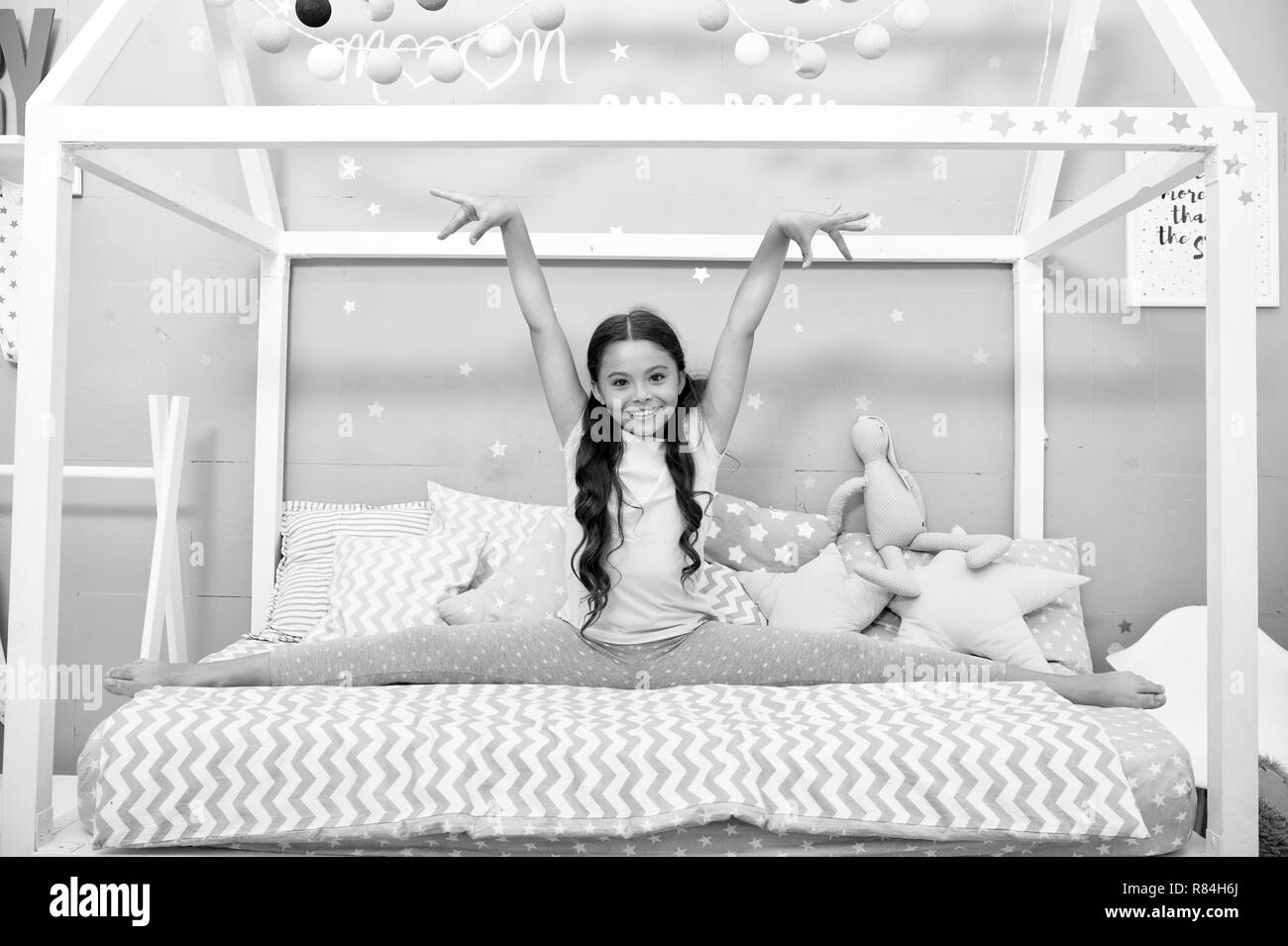 Cute gymnast Praxis split vor dem zu Bett gehen. Mädchen sitzen Bett in  ihrem Schlafzimmer aufgeteilt. Kind vorbereiten, ins Bett zu gehen. Zeit  für den Abend ausdehnen. Mädchen Junge lange Haare niedliche