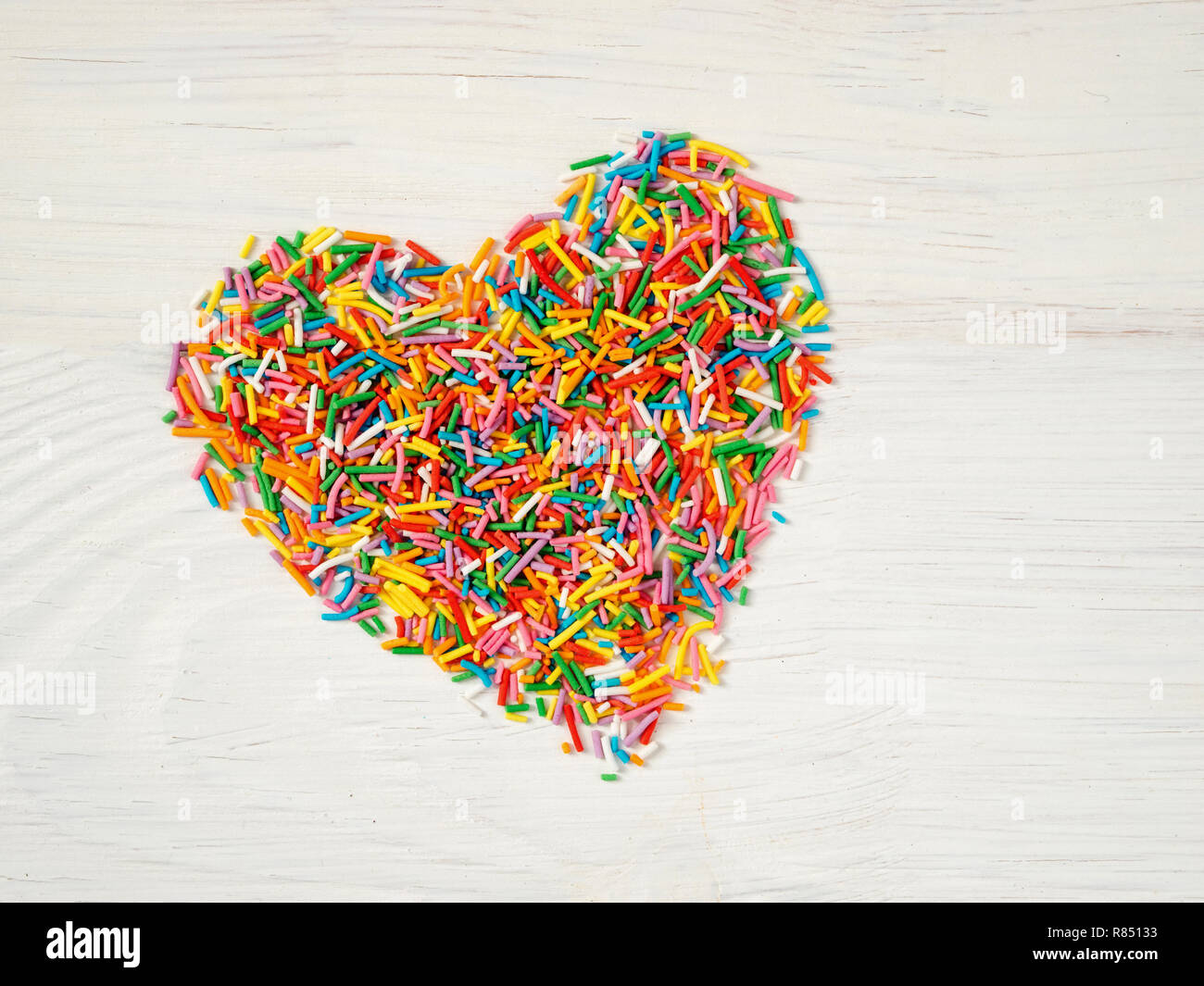 Candy besprüht Form Herz Form. Bunte Herz-Form von candy Konfetti auf weißem Holz- Hintergrund. Valentines Tag Konzept. Top View oder flach Stockfoto