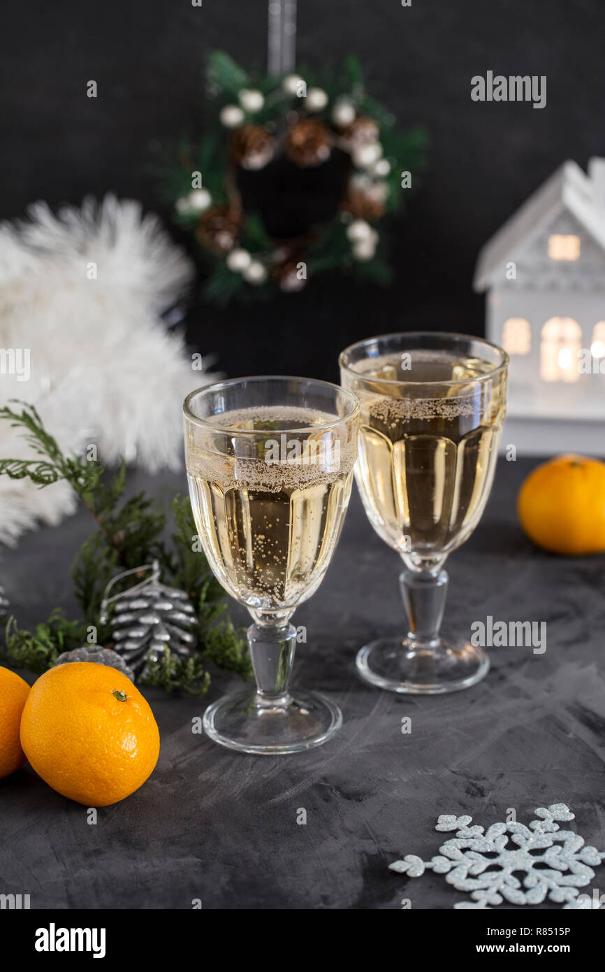 Zwei Gläser mit Champagner bei grauer Hintergrund, Lametta, Mandarinen, Kegel und Weihnachten Spielzeug in der Nähe. Weihnachten Zusammensetzung Stockfoto