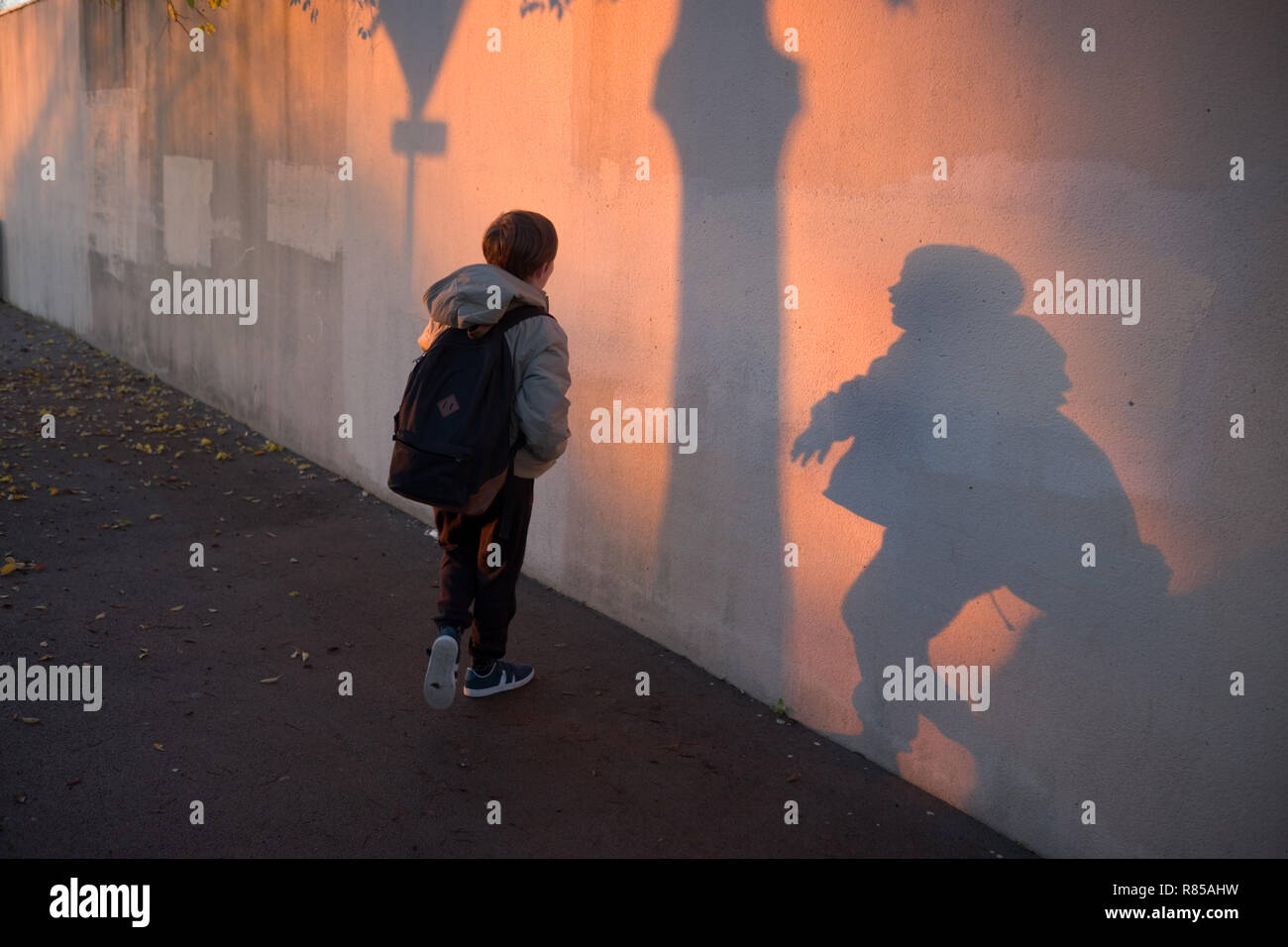 Am frühen Morgen des 11 Jahre alten Junge mit Schultasche spielen mit seinen Schatten an der Wand auf dem Weg zur Hochschule Stockfoto