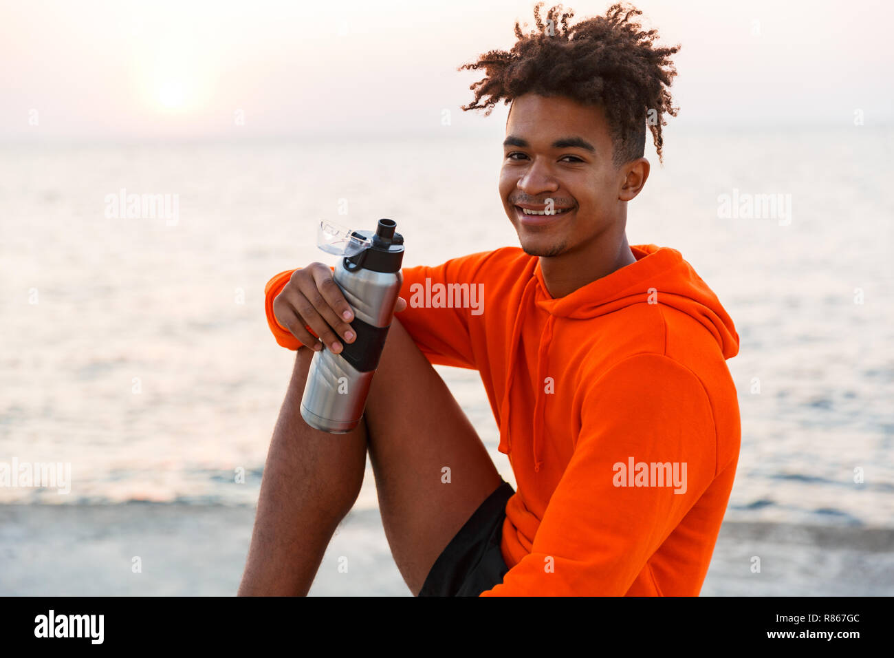 Bild eines fröhlichen jungen afrikanischen Kerl draußen am Strand Trinkwasser. Stockfoto