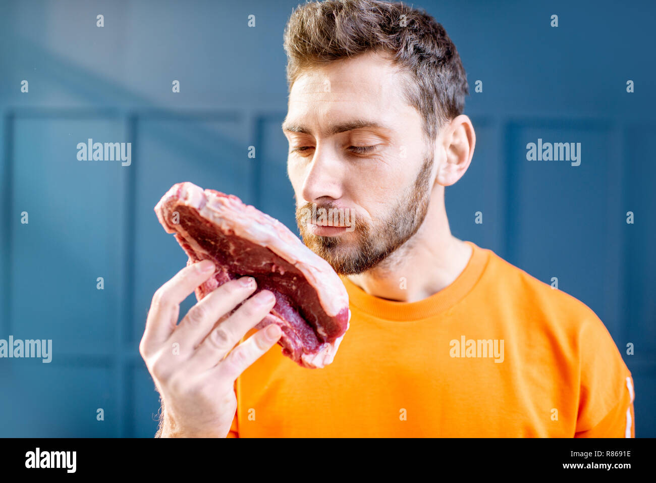 Konzeptionelle Porträt eines Mannes im hellen Pullover mit rohem Fleisch Steak auf dem blauen Hintergrund gekleidet Stockfoto