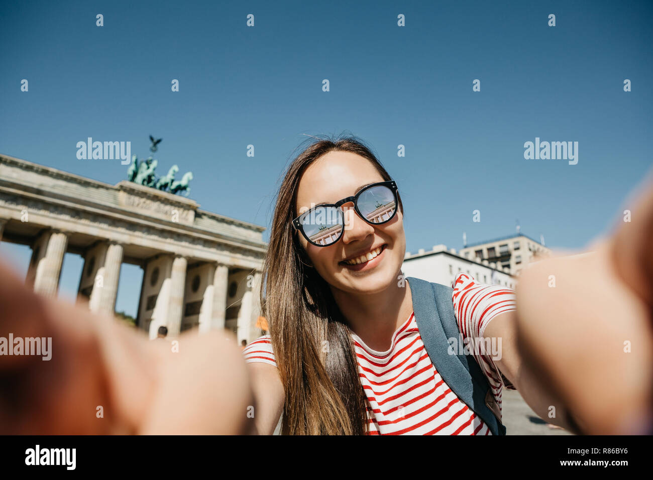 Junge schöne positive Mädchen macht selfie vor dem Hintergrund des Brandenburger Tor in Berlin in Deutschland oder nimmt Bilder von Sehenswürdigkeiten. Stockfoto