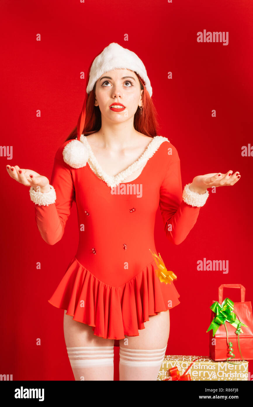 Junge und hübsche rote Kopf Mädchen in einem Weihnachtsmann Mini Kleid auf einem neutralen roten Hintergrund. Stockfoto