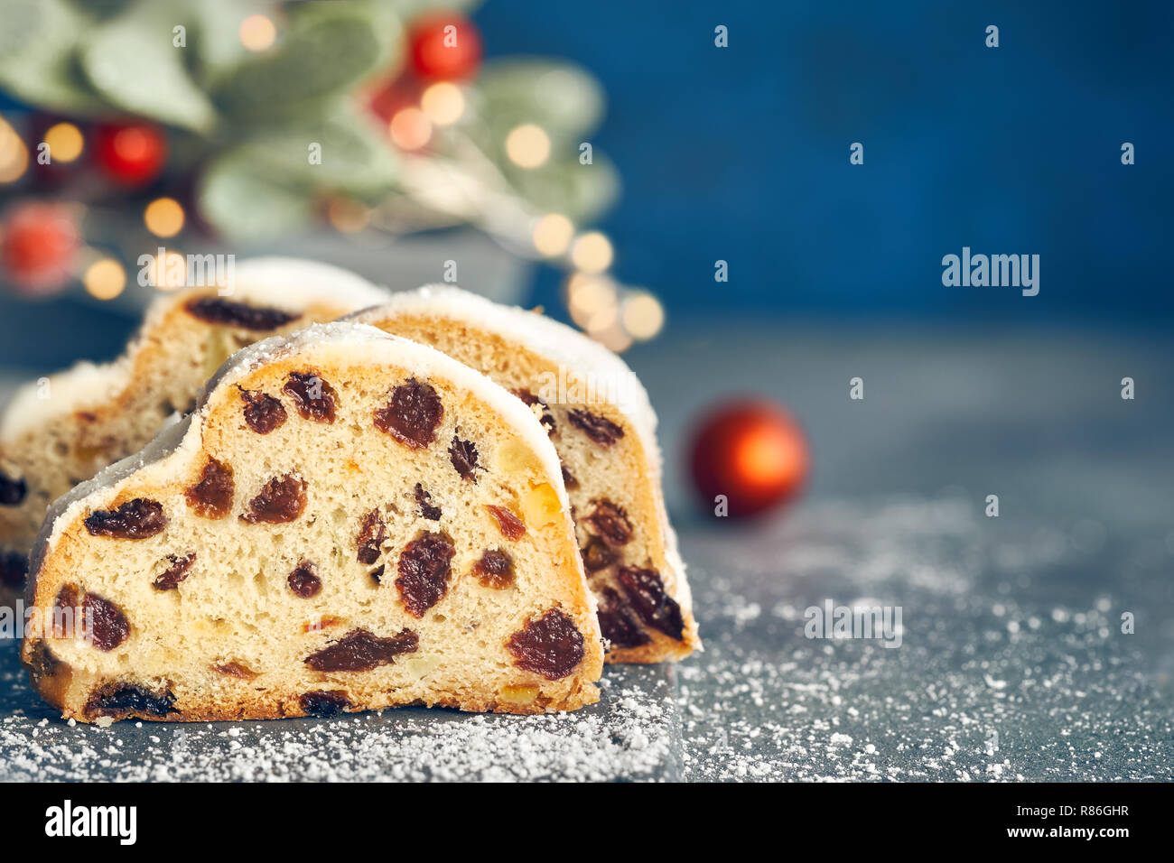 Christstollen auf blau-grünen Hintergrund mit festlichen Weihnachtsbeleuchtung und roten Beeren im Winter, kopieren - Raum. Traditionelle deutsche Dessert für Weihnachten celeb Stockfoto