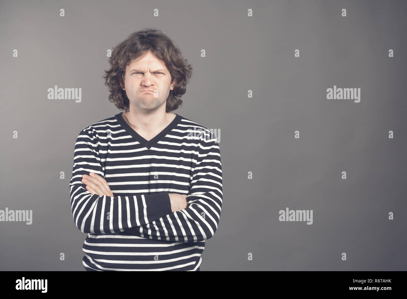Junger stattlicher Mann mit zotteligen Haaren über isolierte grauer Hintergrund Skeptiker und nervös, Missbilligenden Ausdruck auf dem Gesicht mit verschränkten Armen. Negative pro Stockfoto