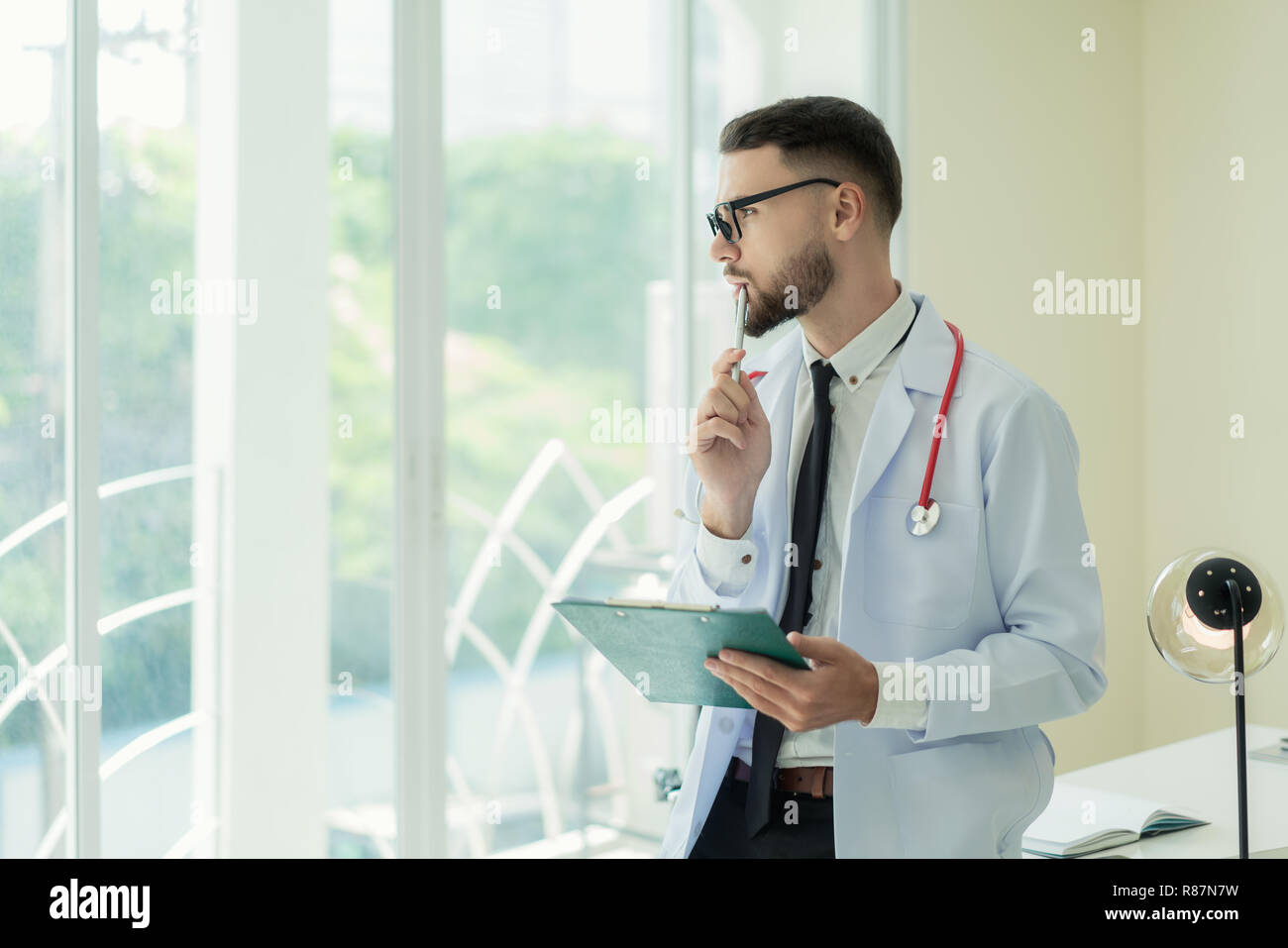 Porträt der jungen kaukasischen männlicher Arzt posiert mit verschränkten Armen und schauen durch das Fenster kopieren. Denken. Stockfoto