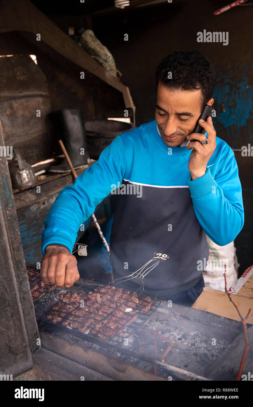 Marokko Errachidia, mann Gespräch am Handy Kochen auf heiße Holzkohle Grill in kleinen Straßenrand Cafe Stockfoto