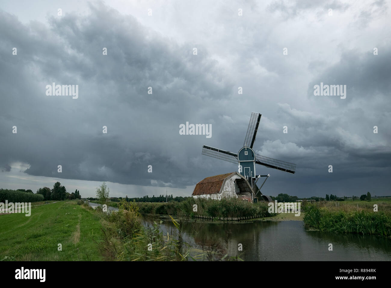 Windmühle in Hazerswoude, Holland unter stürmischen Himmel. Klassische niederländische Szene mit einer Windmühle und Haus an einem Kanal mit dramatischen Wolken im Himmel. Stockfoto