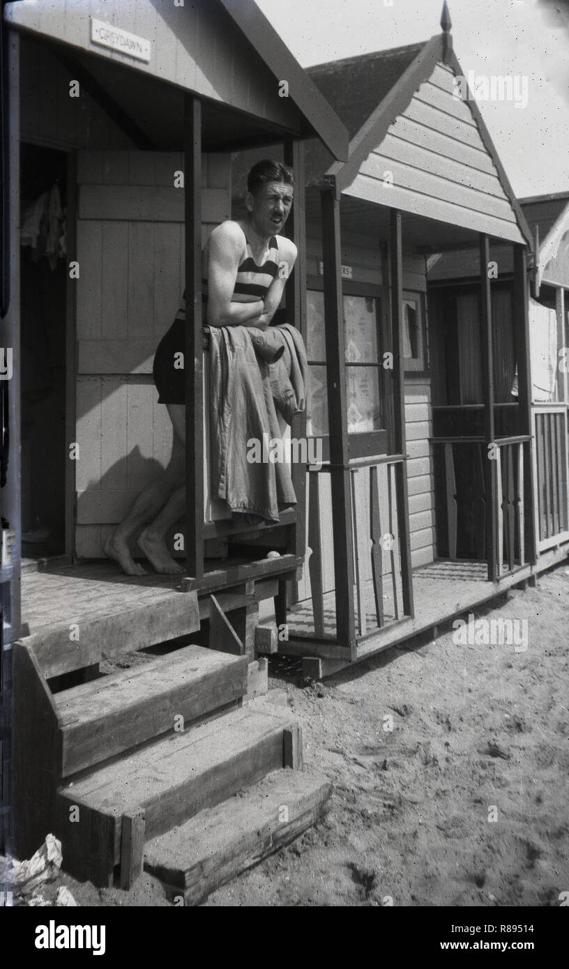 1930er Jahre, ein englischer Mann in ein Streifiges einteiligen sleeveless Badeanzug der Ära, stehend auf der Veranda einer Strandhütte in Southend-on-Sea, England, ein beliebter Ferienort für Menschen in Essex und messetermin London in dieser Zeit leben. Stockfoto