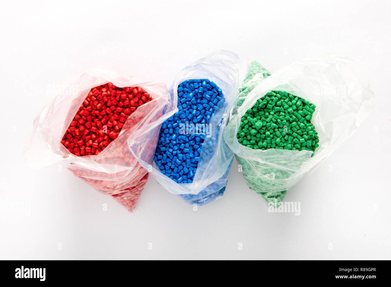 Taschen von bunten Kunststoffgranulat aus roten, blauen und grünen Farben. Von oben auf weißem Hintergrund mit Schatten gesehen Stockfoto